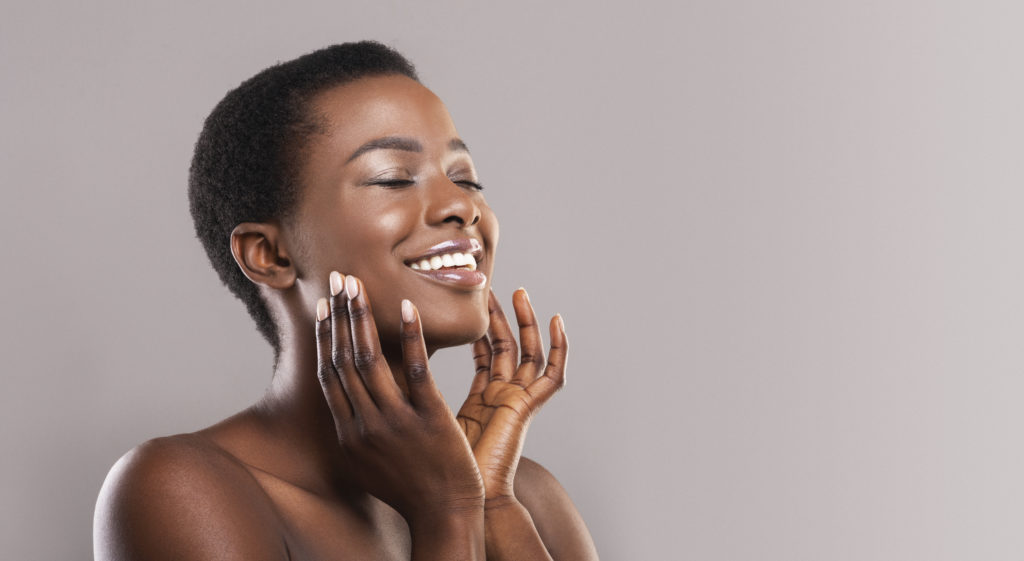 Happy afro woman touching soft smooth skin on her face after JUVEDERM® Injections
