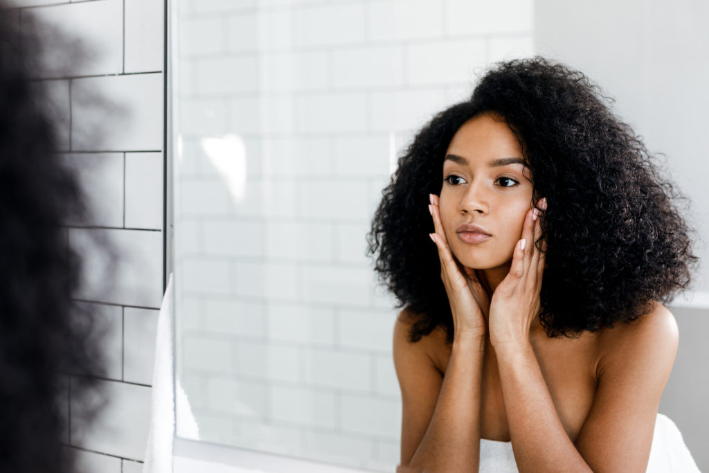 Mixed race woman massaging her face and looking at a mirror